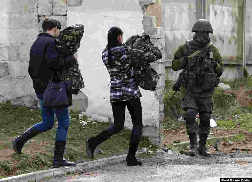 Dve žene za koje se veruje da su iz ukrajinske vojske nose uniforme dok u odlasku iz vojne baze prolaze pored ruskog vojnika 19. marta.