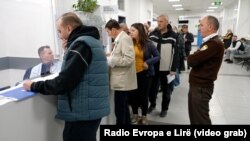Radha e pacientëve para sportelit, ndërsa një pjesëtar i sigurimit qëndron afër tyre.