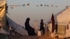 Dečak prolazi pored Palestinke koja sedi u kampu za raseljena lica u pozadini minareta džamije, prvog dana muslimanskog svetog meseca posta Ramazana, u Rafi u južnom pojasu Gaze 11. marta 2024. 