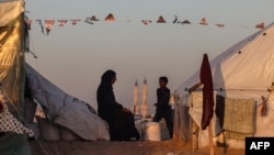 Dečak prolazi pored Palestinke koja sedi u kampu za raseljena lica u pozadini minareta džamije, prvog dana muslimanskog svetog meseca posta Ramazana, u Rafi u južnom pojasu Gaze 11. marta 2024. 