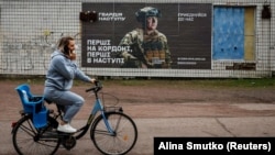 Një banore vendore duke kaluar pranë një afisheje rekrutimi për ushtrinë ukrainase në rajonin Dnipropetrovsk, Ukrainë. Fotografi ilustruese.