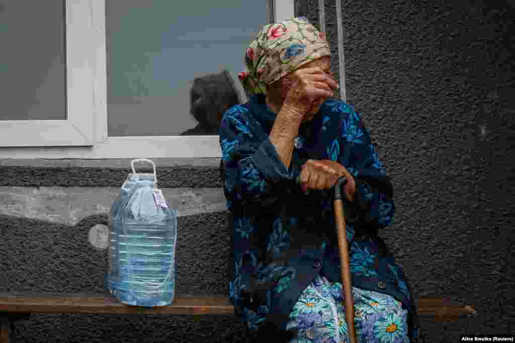 Mai departe, de-a lungul fluviului Nipru, Hanna, o locuitoare în vârstă din satul Hrușivka, stă lângă bidoanele de apă primite ca ajutor.
