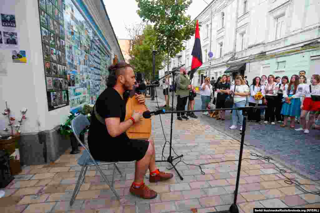 Ukrajinski muzičar svira pored zida posvećenog nekim od Ukrajinaca poginulim u ratu.