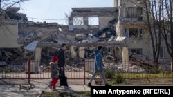 Locuitori ai orașului ucrainean Herson, trecând pe lângă clădirea distrusă de bombardamente a Academiei de Educație Continuă, martie 2024 