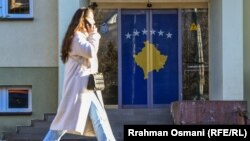 Një kalimtare rasti duke ecur ndërsa në dyert e një objekti është vendosur një flamur i Kosovës. 