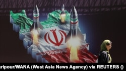 Një grua në Teheran kalon pranë një baneri kundër Izraelit, ku shfaqen edhe raketat iraniane. 19 prill 2024. 