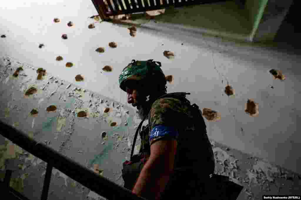 Un soldat urcă scările Casei de Cultură din Blahodatne cu zidurile ciuruite de gloanțe.