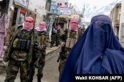 Luptătorii talibani stau de pază în timp ce o femeie afgană îmbrăcată în burqa se plimbă pe o stradă din provincia nordică Badakhshan în februarie.