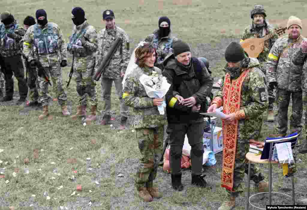 Lesia Ivashchenko dhe Valeriy Fylymonov, të dy anëtarë të Forcave të Mbrojtjes Territoriale të Ukrainës, duke dëgjuar një prift gjatë dasmës së tyre në një pikë kontrolli në Kiev, më 6 mars.