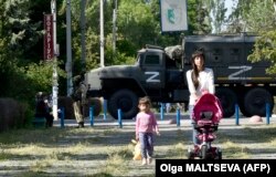 Žena i dijete šetaju parkom dok ruski vojnici patroliraju u Skadovsku u oblasti Herson u okupiranoj Ukrajini