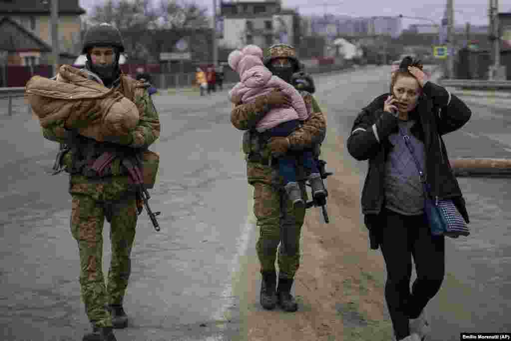 Украински войници носят бебета и помагат на бягащо семейство да намери превоз, след като е пресякло река Ирпин в покрайнините на Киев, 5 март.