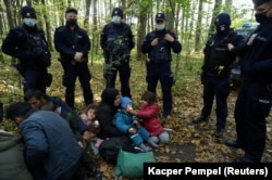 O femeie migrantă irakiană și copiii ei în Hajnowka, înconjurați de polițiștii de frontieră și ofițerii de poliție polonezi, pe 14 octombrie.