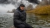 Рибар от Херсон на фона на черния дим от горяща петролна база, 20 ноември 2022 г.
