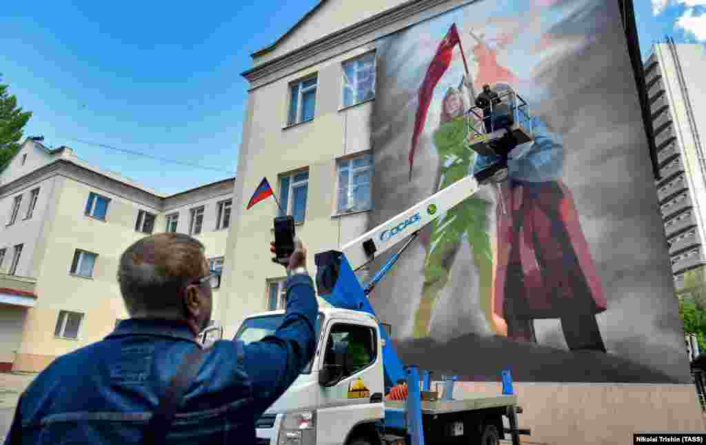 Un pictor lucrează la o pictură murală care face legătura între Al Doilea Război Mondial și invazia rusă în Ucraina, în orașul ucrainean Donețk, ocupat de Rusia, în luna mai.
