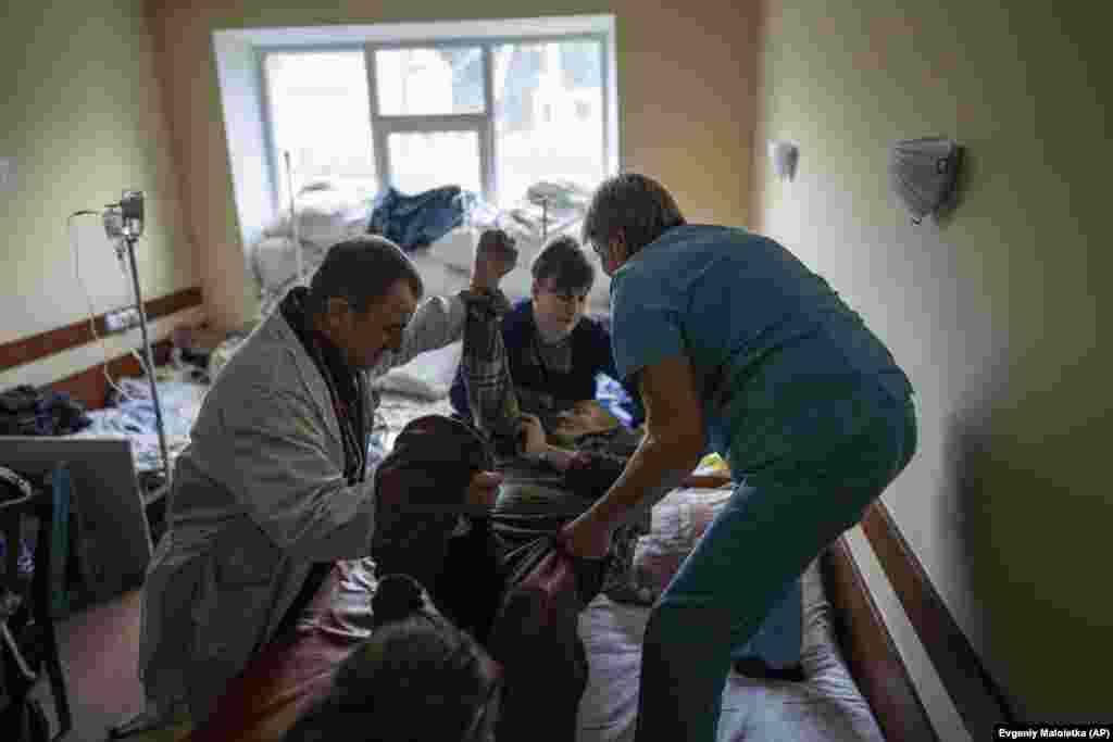 Доктор Јуриј Кузњецов (лево), трауматолог, им помага на медицинските сестри да го преместат пациентот на кревет. Неколкуте лекари, медицински сестри, болничари и патолози кои останаа за време на руската окупација беа единствената надеж за жителите на Изум.