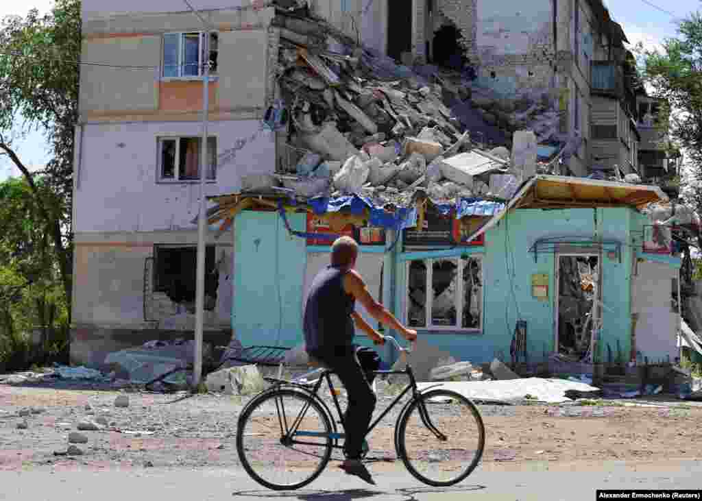 Un localnic pe bicicletă trece pe lângă un bloc grav afectat de focurile de artilerie rusești din Severodonețk, Ucraina. Fotografie realizată la data de 30 iunie 2022.&nbsp;