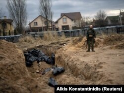 Një foto e bërë më 6 prill tregon një ushtar ukrainas pranë një varri masiv ku ishin varrosur civilët e vrarë gjatë pushtimit rus në Buça.