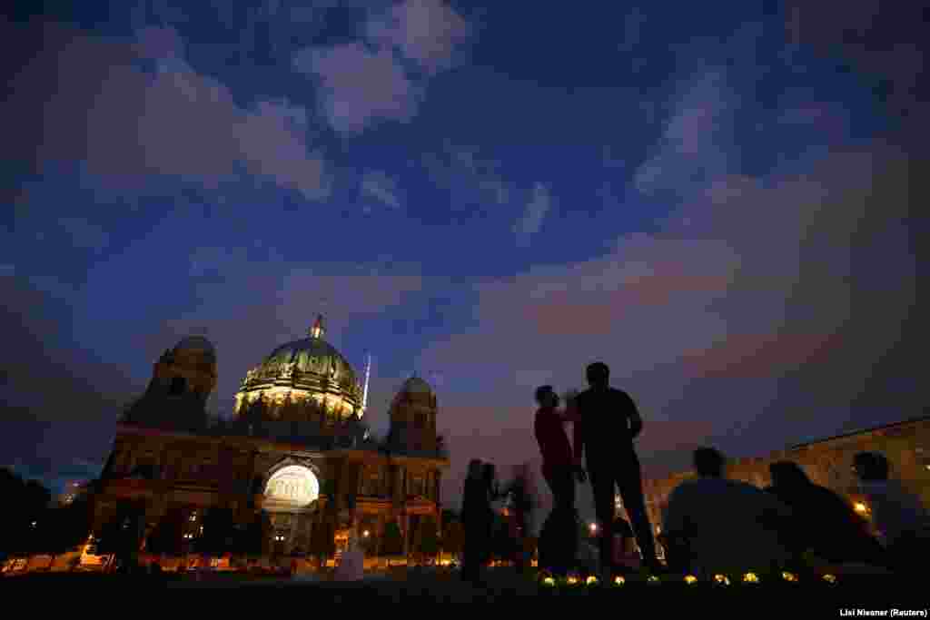 Și în Berlin, monumentele istorice sunt, în mare parte, neiluminate după apusul soarelui. Oamenii se bucură de o seară de vară lângă catedrala din centrul BerlinULUI. 