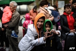 O refugiată ucraineană arată semnul inimii în timp ce așteaptă să se îmbarce împreună cu fiul ei într-un autobuz cu destinația Germania. Capitala Moldovei, Chișinău, pe 13 aprilie 2022.