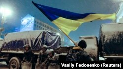 Demonstrant drži ukrajinsku zastavu dok stoji pored pripadnika Ministarstva unutrašnjih poslova 9. decembra. Pripadnici specijalne policije nisu uspjeli da maknu hiljade demonstranata, usprkos oštroj zimi.