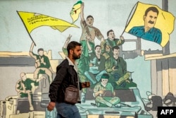 Un bărbat trece pe lângă o pictură murală înfățișând susținători ai forțelor kurde FDS în orașul Qamishli din nord-estul Siriei, pe 16 decembrie.
