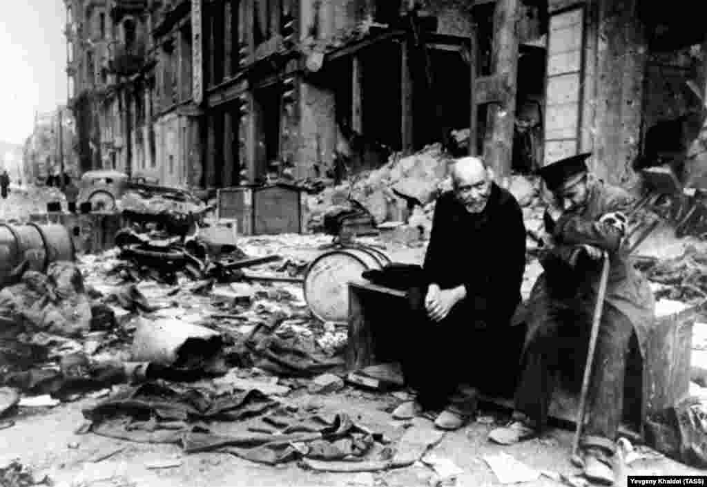 Un bărbat orb (dreapta) cu însoțitorul său pe o stradă în ruine din Berlin în 1945. Khaldei își amintește că i-a întrebat pe cei doi în germană de unde vin. Orbul a răspuns: &bdquo;Nici nu mai știm. Nu știm de unde venim, și nici unde mergem&rdquo;.