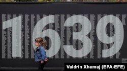 Një vajzë e vogël kalon pranë një bilbordi ku janë shkruar emrat e personave të pagjetur që nga lufta e fundit në Kosovë. Prishtinë, 29 prill 2021. 