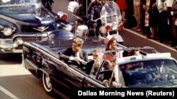 Presidenti John F. Kennedy, duke lëvizur me limuzinën presidenciale, i fotografuar disa minuta para se të qëllohej për vdekje në Dallas të Teksasit më 22 nëntor 1963.