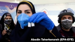 Egy iráni egészségügyi dolgozó az iráni COV Iran Barkat vakcinával egy sajtótájékoztató előtt, amelyen bejelentették a hazai gyártású oltóanyaggal folytatott klinikai kísérletek második és harmadik fázisának kezdetét 2021. március 15-én