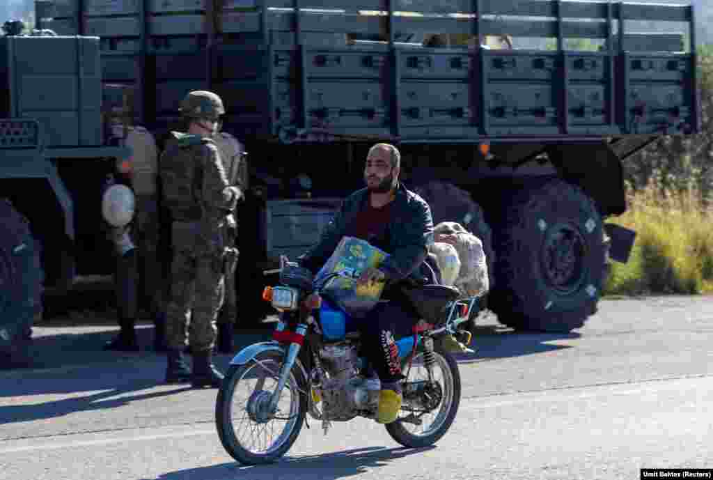 Një banor vendas kalon pranë një autokolone ruse pranë bazës ajrore Hmeimim. &quot;Vendasit vetëm po shikojnë&quot;, thotë Bektas për situatën rreth bazës, e cila tani është pa mbrojtje të jashtme ushtarake përgjatë perimetrit të saj. &quot;Ka shumë dyqane me alfabetin rus në to në fshatin afër bazës ajrore&quot;, tregon Bektas, por të gjitha tani janë mbyllur. &quot;Nuk ka asnjë ushtar rus që del vetëm ose me makinë jo të blinduar apo diçka të tillë&quot;.