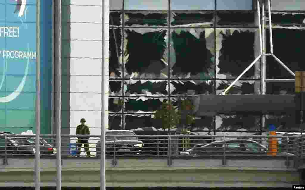 Një ushtar qëndron pranë dritareve të thyera, pas shpërthimeve në aeroportin Zaventem të Brukselit, më 22 mars, 2016.