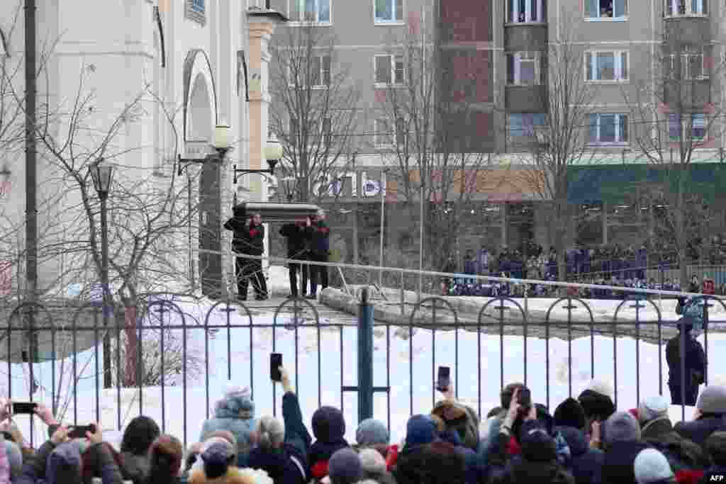 Angajații pompelor funebre poartă sicriul, sub privirile mulțimii.&nbsp;