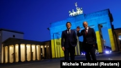 Kancelari gjerman, Olaf Scholz, dhe presidenti francez, Emmanuel Macron, pranë Portës së Brandenburgut, e ndriçuar me ngjyrat e flamurit ukrainas. Berlin, 9 maj 2022.