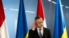 Szijjártó Péter külügyminiszter az ukrán és a magyar zászló előtt hallgatja az ukrán tolmácsot Ungvárban 2024. január 29-én