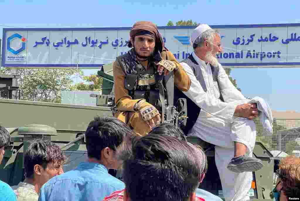A member of the Taliban (left) sits on an armored vehicle observing the dramatic scenes outside the airport in Kabul. 