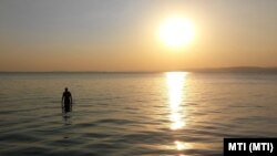 Egy fürdőző besétál az októberi Balatonba és onnan nézi a tó víztükrén csillogó aranyhidat 2017. október elsején
