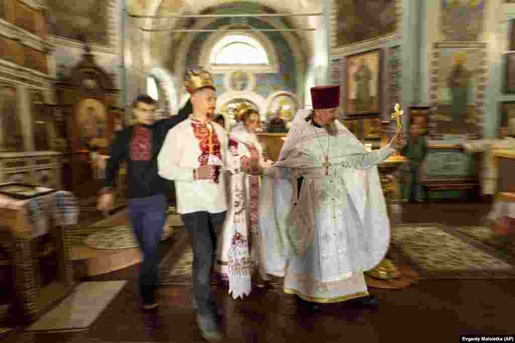 Ushtari ukrainas &quot;Karp&quot; dhe gruaja e tij, Anna, një vullnetare, udhëhiqen nga një prift gjatë ceremonisë së tyre martesore në rajonin e Harkivit më 24 korrik. Rritja masive e dasmave në Ukrainë ka precedent historik. Në kulmin e Luftës së Dytë Botërore në vitin 1942, Shtetet e Bashkuara regjistruan 1.8 milion dasma në 12 muaj - një rritje prej 83 për qind krahasuar me një dekadë më parë.