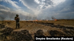 Un militar ucrainean la marginea unui lan de grâu în flăcări, în apropierea frontului, la granița dintre regiunile Zaporojie și Donețk, 17 iulie 2022