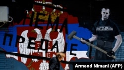 Koszovói szerb asszony sétál el egy graffiti előtt, amelyen a szerb zászló alatt a Nem adjuk fel felirat áll Mitrovica főként szerbek lakta, északi részében. 2021. június 15.