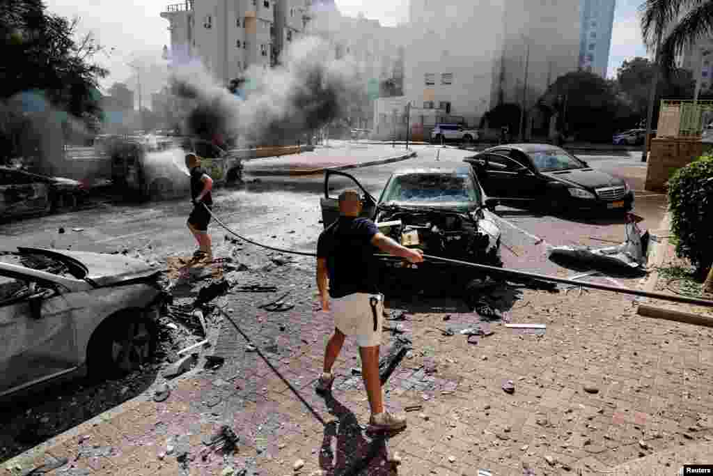 Qytetarët shuajnë makinat e djegura, që u goditën nga raketat e lëshuara nga Gaza. Ashkelon, 7 tetor 2023.&nbsp;