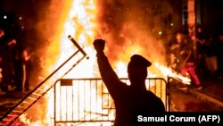 Част от протестите прерастнаха до безредици. На снимката протестиращ е вдигнал ръка в юмрук пред горящ огън във Вашингтон