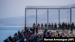 Bevándorlók várnak, hogy bejuthassanak a Marokkó és Spanyolország határához közeli Ceuta spanyol enklávéba, 2021. május 18-án.