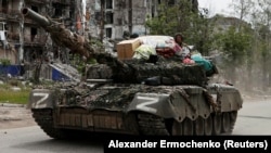 Trupat ruse apo proruse kalojnë me tanke pranë një ndërtese të shkatërruar banimi në qytetin Popasna në rajonin Luhansk, 26 maj 2022.