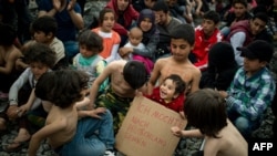 Un copil ține un semn cu mesajul „Vreau să merg în Germania” în tabăra de refugiați Idomeni, martie 2016, în anii de vârf ai „crizei refugiaților”.