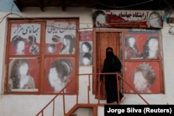 Një grua e mbuluar me nikab hyn në një sallon bukurie, ku reklamave u janë fshehur fytyrat e grave. Kabul, tetor 2021