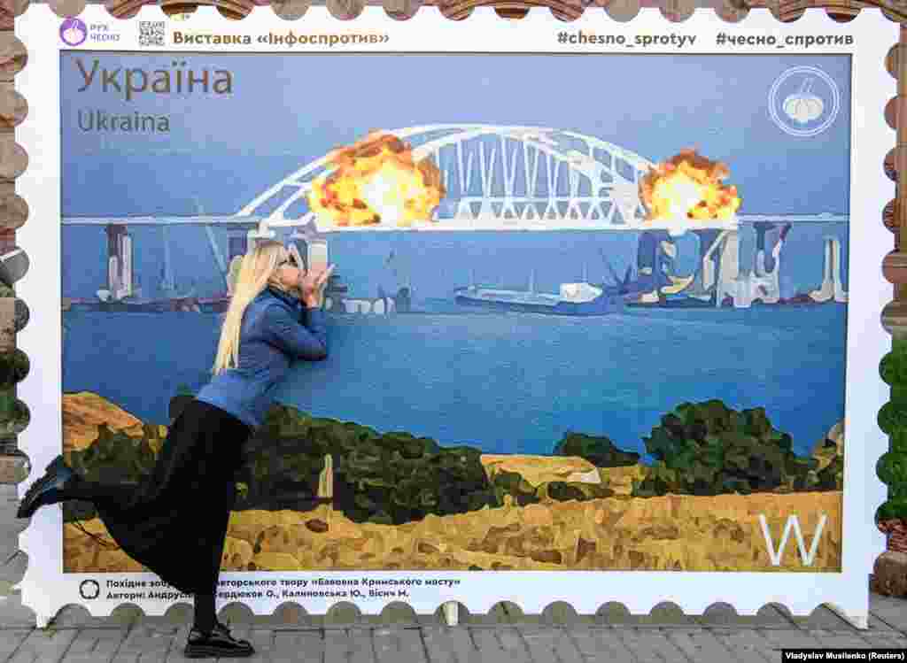 O tânără pozează, în centrul K9evului, lângă un poster care înfățișează Podul Crimeii în flăcări, 8 octombrie.