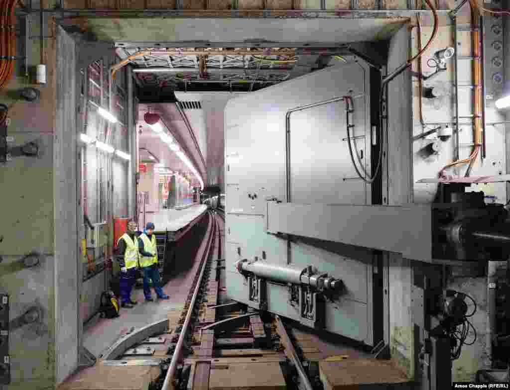 Inxhinierët duke shikuar ndërsa dera rezistente ndaj shpërthimeve me mbyllje hermetike, lëviz mbi shinat e metrosë. Sistemi Mbrojtës i Metrosë u ndërtua në rrjetin e metrosë së Pragës duke filluar nga viti 1974, kur hija e luftës bërthamore po përndiqte Evropën. &nbsp;