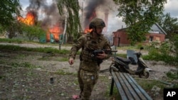 Un polițist din apărarea teritorială ucraineană pe fundalul unei clădiri lovite de o bombă rusească la Vovciansk, pe 11 mai 2024.