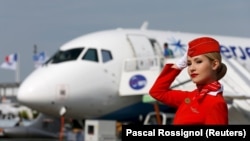 Az Aeroflot orosz légitársaság egyik utaskísérője pózol egy Szuhoj Superjet 100-as repülőgép előtt