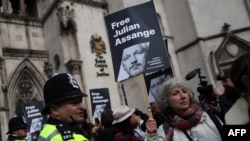 Ofițerii de poliție stau de pază în timp ce susținătorii fondatorului WikiLeaks, Julian Assange, țin pancarte în fața Curții Regale de Justiție, Înalta Curte a Marii Britanii, în centrul Londrei, 26 martie 2024.